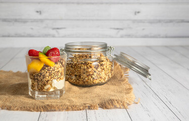 Delicious homemade granola in a glass jar on white wooden background