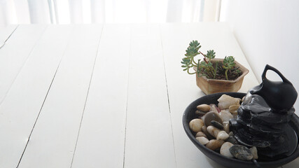 Close view of a zen water fountain with a small succulent plant behind. Placed on top of a white wooden table      