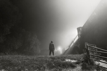 A hooded figure looking up at street lights on the edge of town. On a spooky, foggy night. With a...