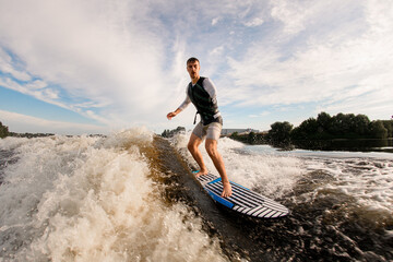 active armless man is surfing on surfboard trails behind boat. Wakesurfing on the river