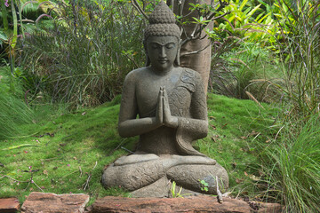 A sculpture of a peaceful praying Buddha in a garden