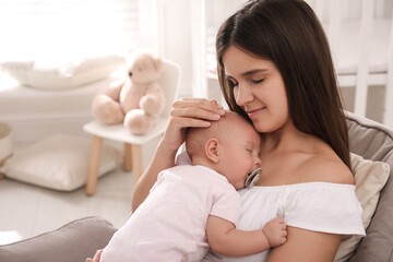 Happy young mother with her sleeping baby in armchair at home