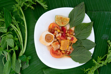 Papaya Salad with Corn and Salted Egg with green leaves of basil arranged on a white plate. Banana leaves and various vegetables for background. Luxurious ready-to-serve meals from Thailand.