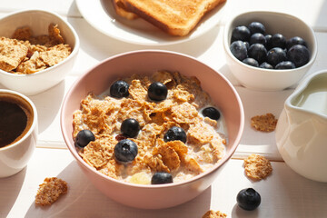 Breakfast of whole wheat flakes with milk, blueberries, coffee and toast close-up on wooden table. Selective focus, morning concept