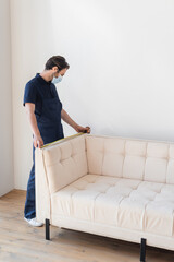 mover in overalls measuring white couch in modern apartment