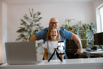 Laughing daughter with funny daddy pose together shooting new video for blog at home
