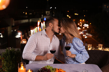 Romantic couple with glasses of red wine kissing on cafe terrace at night