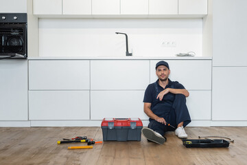 Fototapeta na wymiar handyman in overalls sitting on floor in kitchen near tools and toolbox