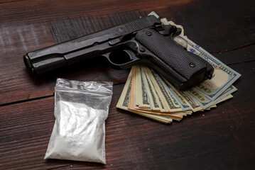 Drugs narcotics business concept. Cocaine plastic packets, gun and US dollars banknotes on a table. White powder addiction and crime