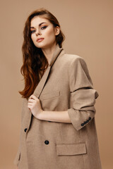 stylish brunette woman in a coat on a beige background straightens the collar