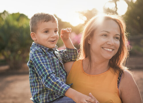 Happy Mother Holding Her Son On Her Arms At City Park - Mother And Child Love