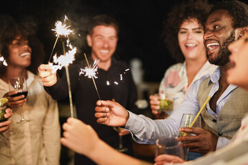 Group of young multiracial people celebrate new year's eve together with sparklers and cocktails