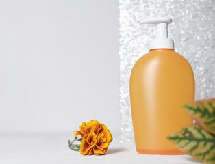 fall cosmetic product in orange container with pump.shower gel or liquid soap next to glass bathroom door and orange flower. fall product sale concept. 