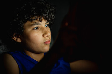 Joven en la oscuridad jugando con un tablet que ilumina su rostros