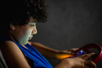 Joven en la oscuridad jugando con un tablet que ilumina su rostros
