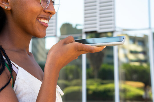 Cheerful black woman recording voice message on smartphone