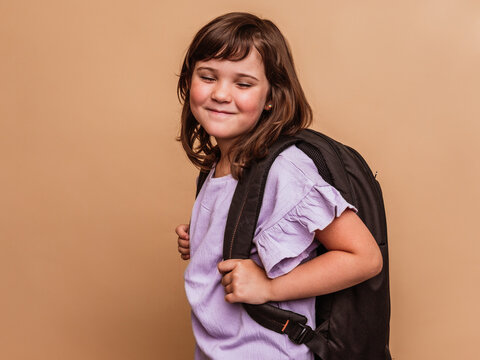 Charming girl with backpack on brown background