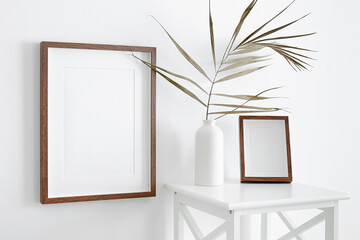 Blank portrait frames mockup on white wall with furniture and dry palm leaf decorations in vase. Minimalistics style interior with artwork mockup.