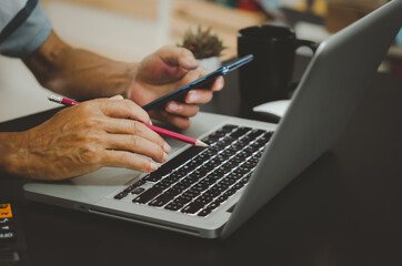 Hand holding a pencil, calculator and mobile phone, computer keyboard on the desk.