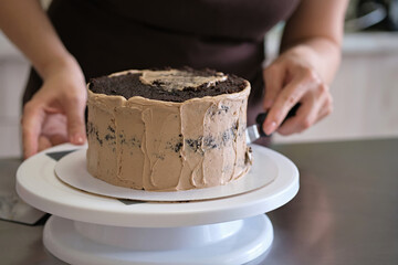 Woman pastry chef making chocolate cake with chocolate cream, close-up. Cake making process, Selective focus