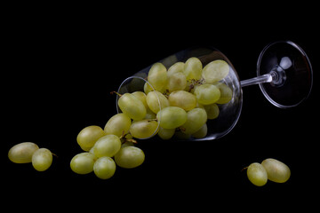 A wine glass filled with green grapes lies on a black background.