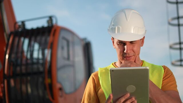 worker in hard a hat with digital tablet near excavator. construction site driver with digital tablet. industry construction concept. worker in hard hat near excavator truck in business uniform.