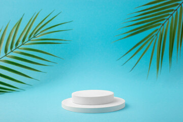 Fototapeta premium White podium for product presentation with tropical leaves on blue background. Skincare products , natural cosmetic. Beauty concept for face and body care. Empty cylindrical platform for cosmetic