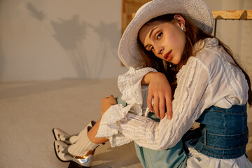Fashionable woman wearing trendy  white hat, vintage shirt, denim corset, cowboy boots. Model...