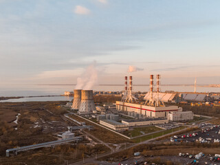 Obraz premium Thermal power plant on sunset. Heat generation for heating on cold days, environmental pollution. Baltic sea on the background. Industrial zone. Save earth concept. Aerial view. Blue sky.