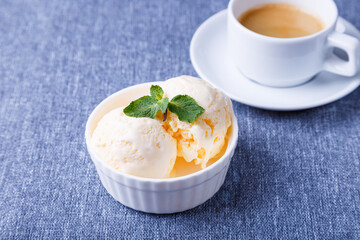 Vanilla ice cream with mint in a white plate and a cup of espresso on a blue background. Homemade ice cream. Close-up.