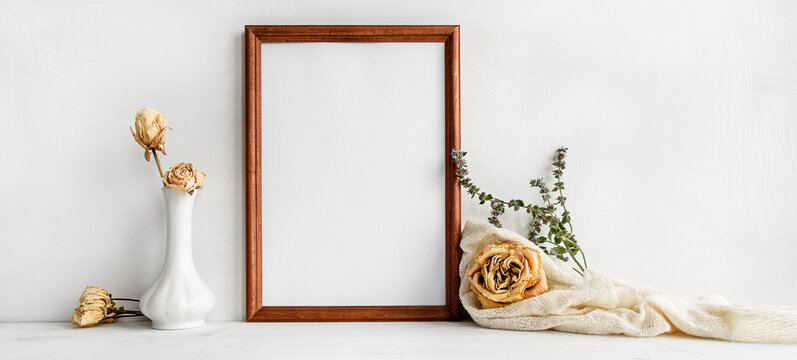 A wooden empty photo frame on a white table and flowers in a vase. A fashionable wedding or holiday banner.
