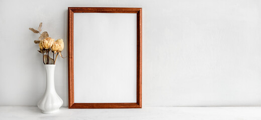 A wooden empty photo frame on a white table and flowers in a vase. A fashionable wedding or holiday banner.