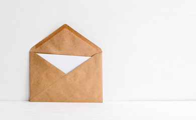 An envelope made of kraft paper and a white empty card inside on a white table. Blank or empty...