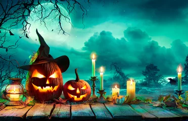 Fototapeten Halloween bei Nacht - Kürbisse mit Hexenhut und Kerzen auf dem Tisch in einer mysteriösen Landschaft © Romolo Tavani