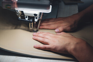 Working process of leather craftsman. Tanner sews leather on a special sewing machine, close up.