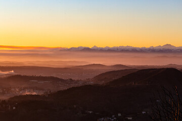 View of the misty and fog surrounding the mountains of the Italian Alps at winter sunset. Layers of mountains. Nature tourism.