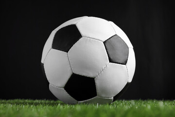 Fototapeta na wymiar Football ball on green grass against black background