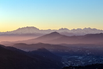 View of the misty and fog surrounding the mountains of the Italian Alps at winter sunset. Layers of mountains. Nature tourism.