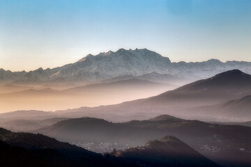 Fototapeta na wymiar View of the misty and fog surrounding the mountains of the Italian Alps at winter sunset. Layers of mountains. Nature tourism.