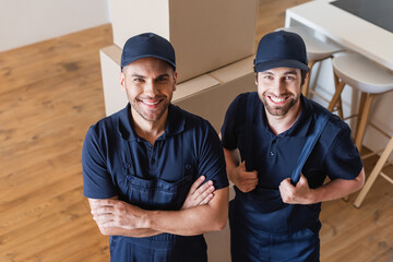high angle view of joyful movers smiling at camera near carton boxes
