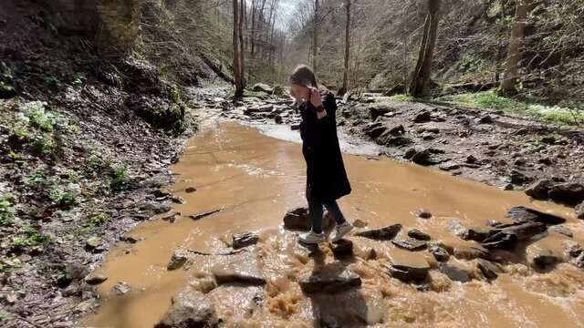 Female tourist cross river carefully on stones. Young woman overcomes obstacles in hike
