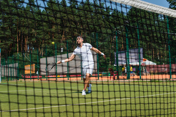 Sportsman playing tennis on court near blurred net