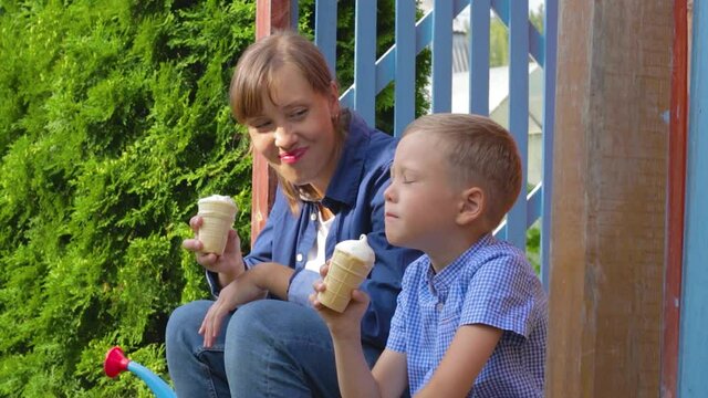 Preschooler boy with mom eating ice cream on the porch of a house in the village on a summer sunny day. Selective focus. Portrait