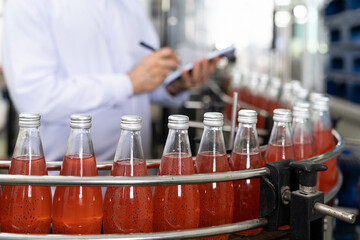 Hands of male factory worker writing notes about product of Basil seed with fruit on the conveyor belt in the beverage factory. Worker checking bottling line for processing. Inspection quality control