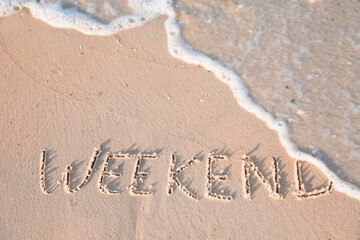 Fototapeta premium Word Weekend written on sand at beach, above view