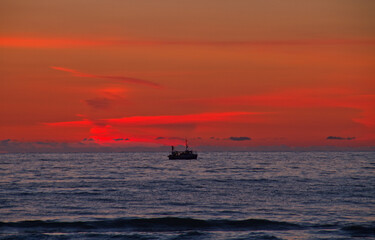 Silhouette of fishing boat on calm sea just after sunset
