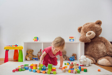 Sweet happy child boy having fun at home playing with his giant teddy bear and colorful wooden blocks and toys, on the floor.