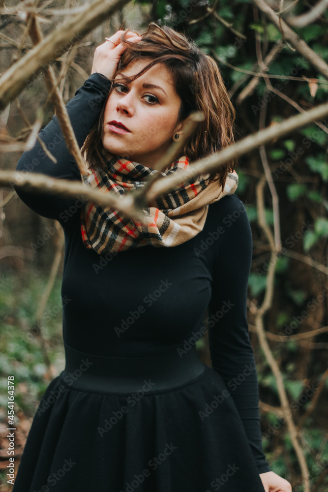 Poster Vertical shot of a Caucasian female dressed in a black dress and a scarf in the forest in autumn