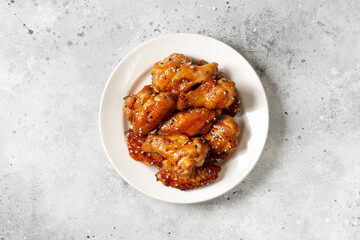 Homemade baked or fried chicken wings in barbecue sauce in a plate on a light gray cooking table top view	
