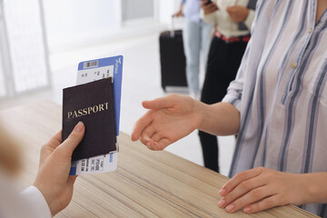 Agent giving passport with ticket to client at check-in desk in airport, closeup